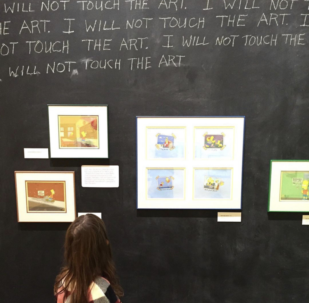 A small child looks up at works on view in Bart at TAM: Animating America's Favorite Family.