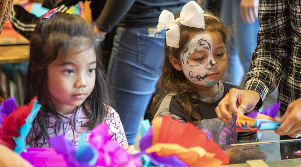 Two children assemble paper flowers during the Dia de los Muertos community festival.