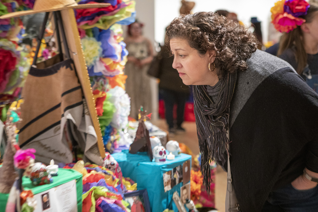 Woman leans over to look closely at an altar set up during TAM's Dia de los Muertos community festival.