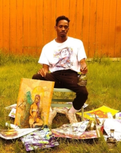 Artist Perry Porter sits in a grassy yard surrounded by his work and painting supplies. 