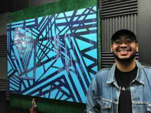 Artist Jalen Calhoun stands in front of an abstract painting he created. 