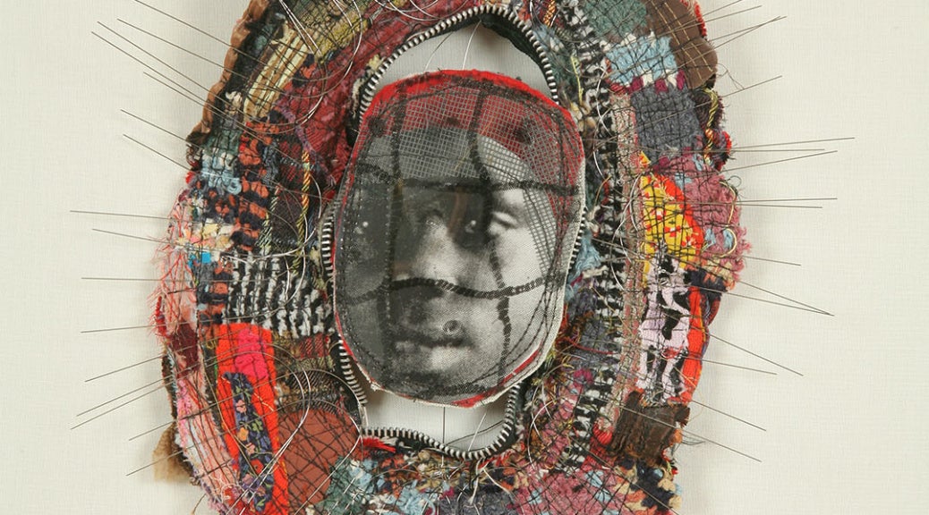 Small brooch-like sculpture with a photo of a young African American girl at center surrounded by a border of wire and cloth fragments.