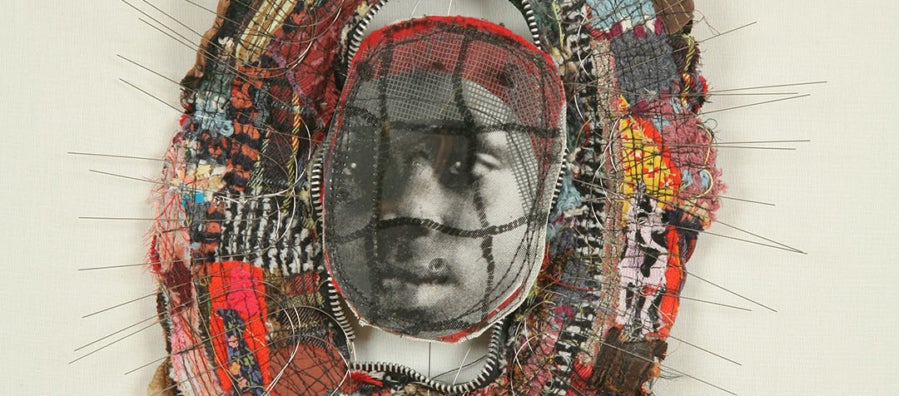Small brooch-like sculpture with a photo of a young African American girl at center surrounded by a border of wire and cloth fragments.