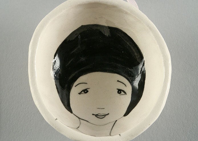 Single vessel from the Waiting Lady series. Shallow, small white porcelain bowl with the face of a female figure in black line on the interior.