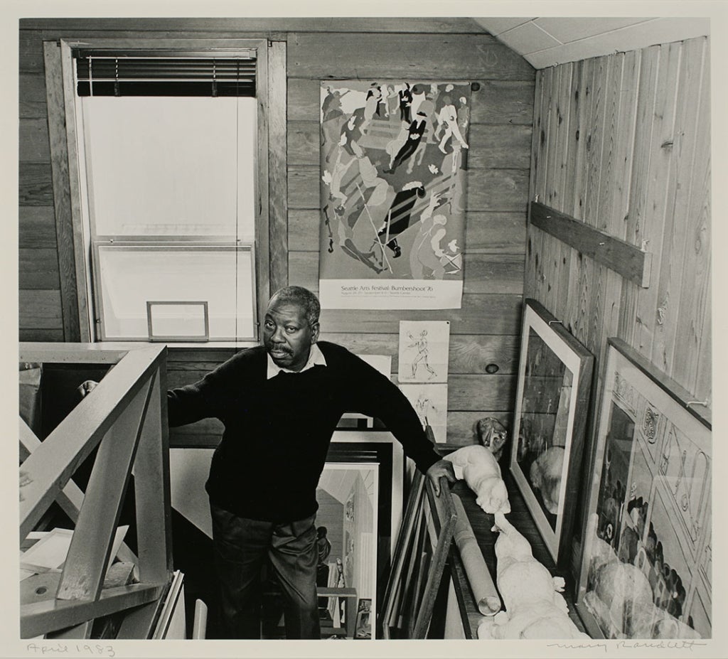 Black and white portrait of the artist, Jacob Lawrence standing on the stairs up to his loft studio.