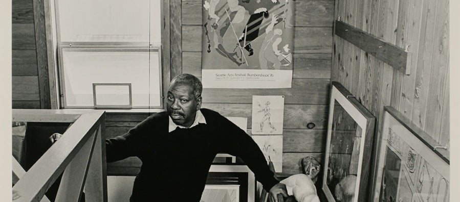 Black and white portrait of the artist, Jacob Lawrence standing on the stairs up to his loft studio.
