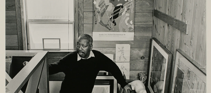 Black and white portrait of the artist, Jacob Lawrence standing on the stairs up to his loft studio.