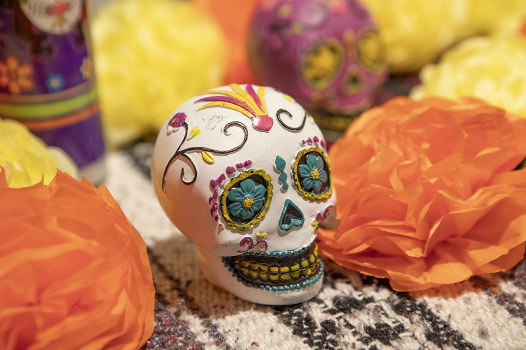Small ornate skull decorated with green eyes, green around the nose, and a large smiling face. The skull is surrounded by paper flowers.