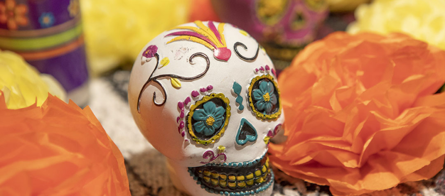 Small ornate skull decorated with green eyes, green around the nose, and a large smiling face. The skull is surrounded by paper flowers.