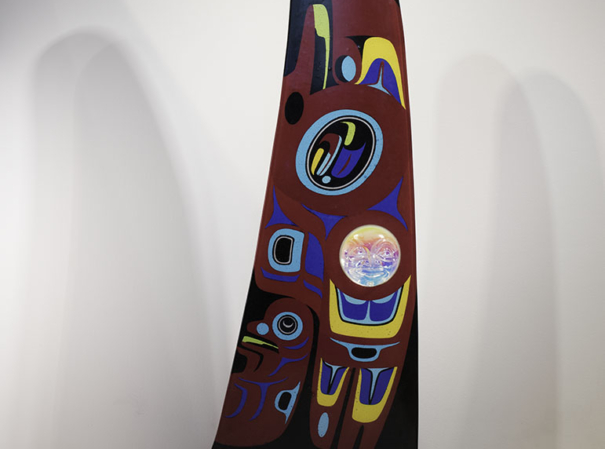 A large fin-shaped piece of glass with a red background, black top, and base made of blue metal wave shapes. The body of the