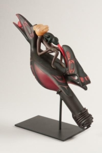 Sculpture of a large, black bird with three figures on its back: a masked human body with a frog-like animal straddling a large bird's (rabbit's?) head. Frog is inserting tongue into bird head's mouth.