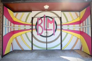 White panels decorated with green, yellow, and pink concentric circles, lines, and "BLM" at the center cover storefront windows.