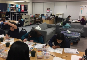 Students sit at tables working on art projects during Sketch Club