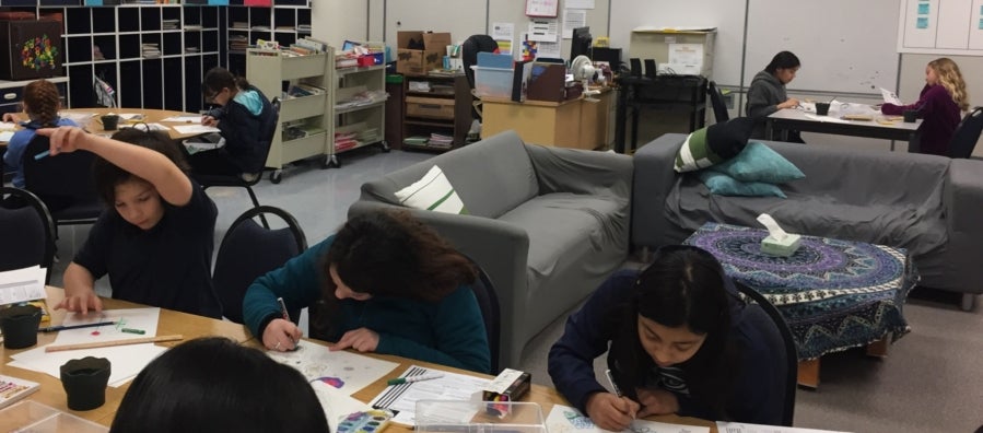 Students sit at tables working on art projects during Sketch Club
