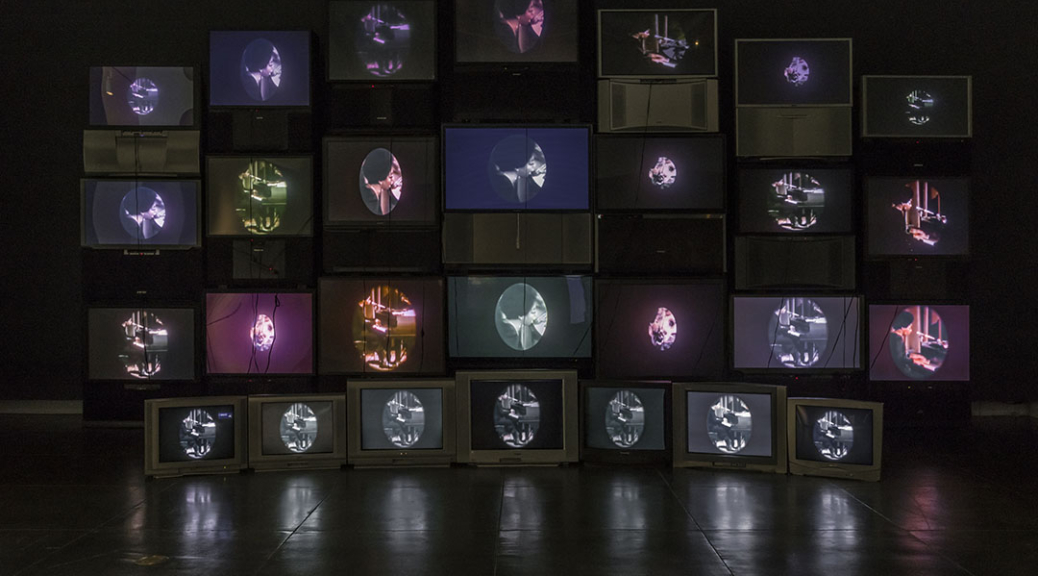 Photograph of video installation exhibition, "Black is the Color," made up of 28 salvaged televisions.