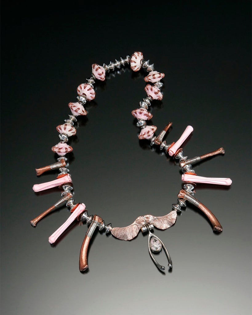 Necklace made of pink plastic hair curler parts held together with copper wire. Copper chicken bones partially wrapped in silver. With silver beads (diamond shaped) in cross section. Wishbone pendant suspended by wing shaped piece. Pink stone at middle.