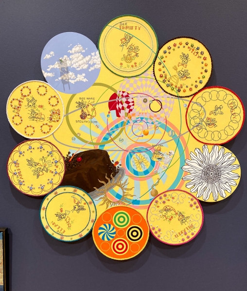 Artwork is composed of a large central circular canvas with a border of smaller circular canvases. All are painted with symbols and geometric shapes against a yellow background.