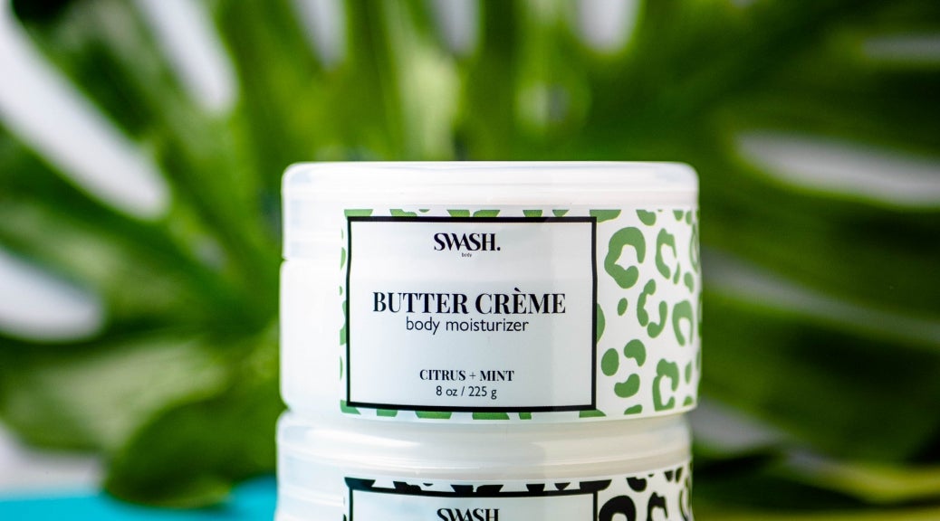 Two containers of SWASH Body moisturizer cream displayed in front of a monstera leaf.