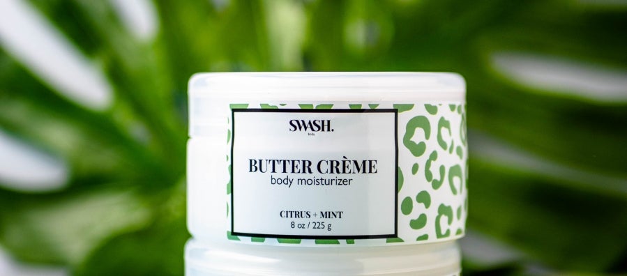 Two containers of SWASH Body moisturizer cream displayed in front of a monstera leaf.