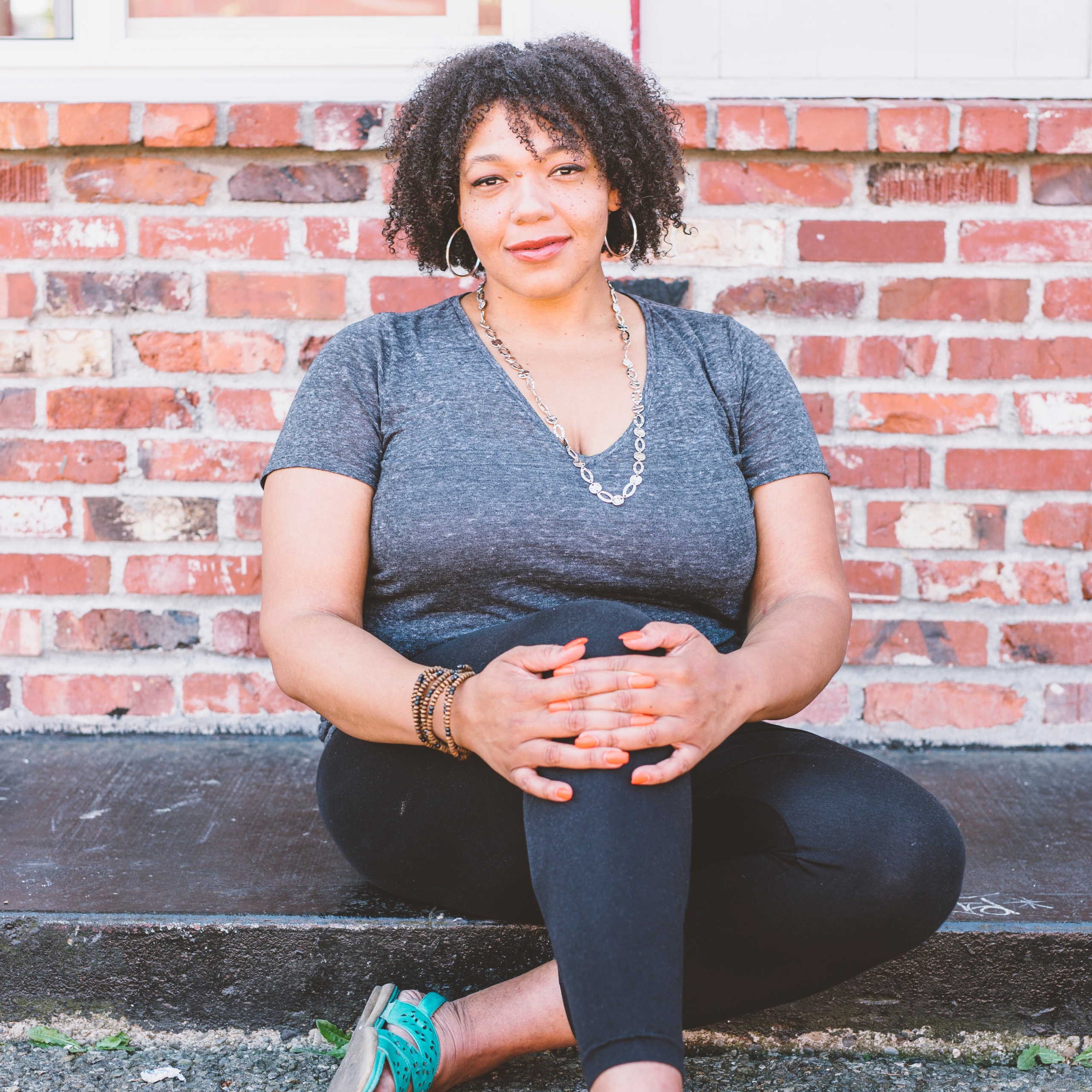 Photo of SWASH Body owner and CEO Aikita Jones posed seated on the sidewalk in front of a brick wall.