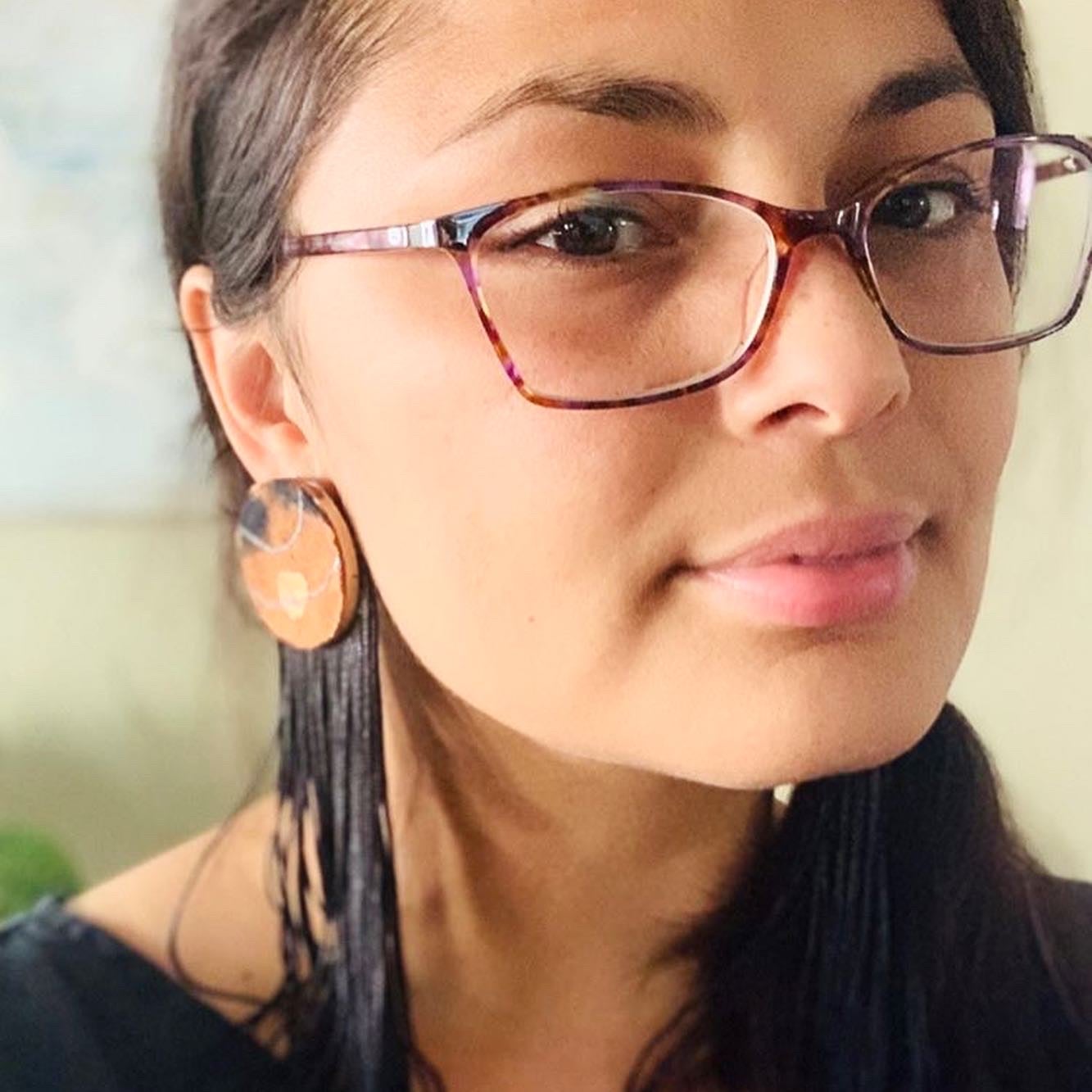 Model with glasses wearing a pair of black and brown fringe earrings.