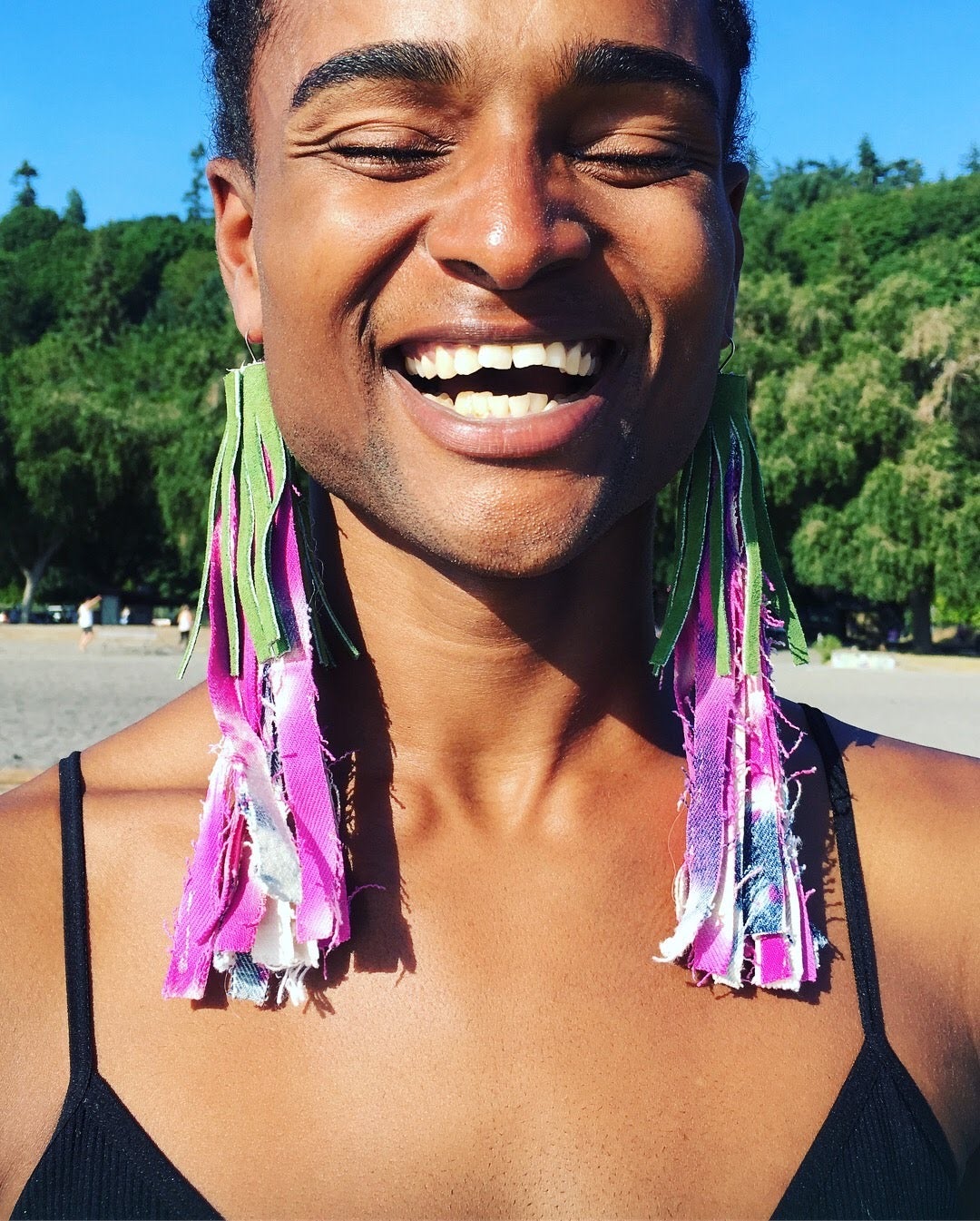 Smiling model posing outside and wearing large, long pink and green tassel earrings.