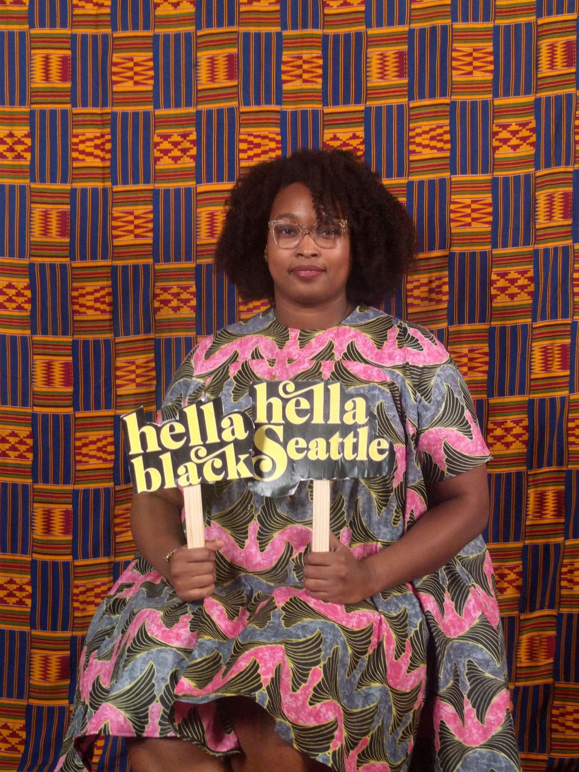 Color photograph of Seattle artist, the monarq posed in front of a quilted background.