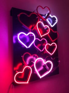 Color photo of neon hearts in various shades of pink and red set against a black background.