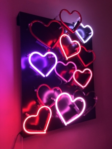 Color photo of neon hearts in various shades of pink and red set against a black background.