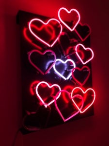 Color photo of neon hearts in various shades of pink and red set against a black background.
