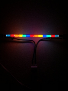 Color photo of a multicolor neon tube hung up against a dark background.