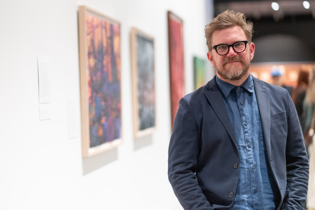 An image of artist Cable Griffith standing in front of his artwork 